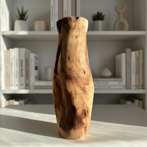May include: A tall, wooden vase with a natural, organic shape. The vase is made from light and dark brown wood, showcasing the grain and knots. It has a wide base and a narrower opening, perfect for displaying flowers or as a decorative piece.