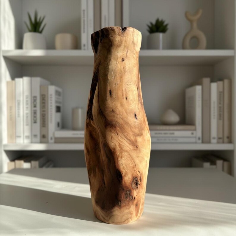 May include: A tall, wooden vase with a natural, organic shape. The vase is made from light and dark brown wood, showcasing the grain and knots. It has a wide base and a narrower opening, perfect for displaying flowers or as a decorative piece.