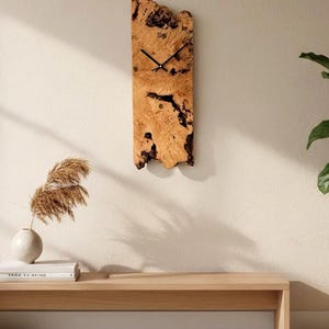 Peut inclure: Une horloge murale rectangulaire en bois avec des aiguilles noires. L'horloge est faite d'un bois clair et texturé avec des accents marron foncé et noirs. L'horloge est fixée sur un mur de couleur claire. Décoration intérieure.