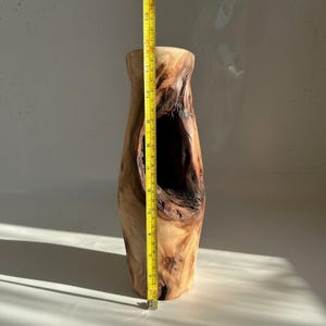 May include: A tall, natural wood vase with a large, irregular opening. The vase is approximately 14 inches tall, with a light brown exterior and darker brown interior. A yellow measuring tape is placed next to the vase.