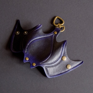 May include: A dark blue leather key chain with a heart-shaped clasp and decorative studs. The key chain is shaped like a bat.