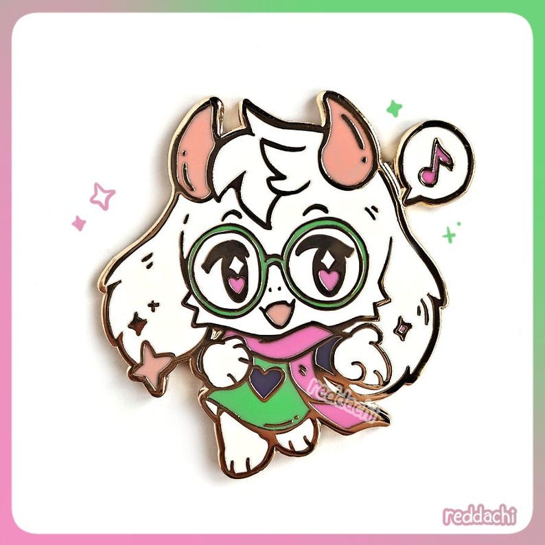 May include: A colorful enamel pin featuring a cartoon character with white fur, pink horns, and green glasses. The character wears a pink scarf and green tunic. A musical note is in a speech bubble. The pin has a gold border and the text "redddachi".