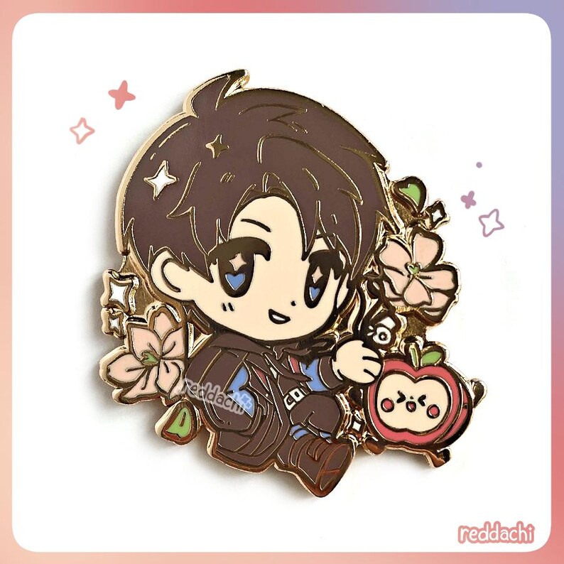 Peut inclure: &Eacute;pinglette en &eacute;mail d&eacute;taill&eacute;e repr&eacute;sentant un personnage de dessin anim&eacute; aux cheveux bruns et une tenue marron, tenant un petit objet. L'&eacute;pingle comprend des fleurs roses et une pomme rouge avec un visage mignon. L'&eacute;pingle porte le texte "reddachi".