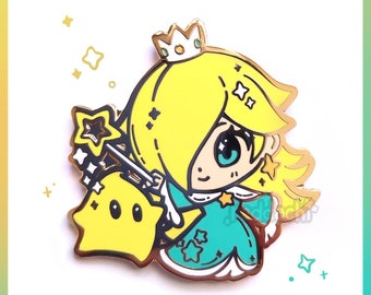May include: A gold-colored enamel pin featuring a cartoon character with yellow hair, a crown, and a teal dress. The character is holding a star-shaped wand and is accompanied by a yellow star-shaped companion. The pin has a glossy finish and the text "reddachi".