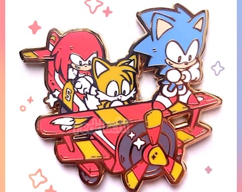 Könnte beinhalten: Ein farbenfroher Emaille-Pin mit Sonic the Hedgehog, Knuckles und Tails in einem roten, gelben und goldenen Flugzeug. Der Pin hat einen goldenen Rand und der Text "redddachi" befindet sich in der unteren rechten Ecke.