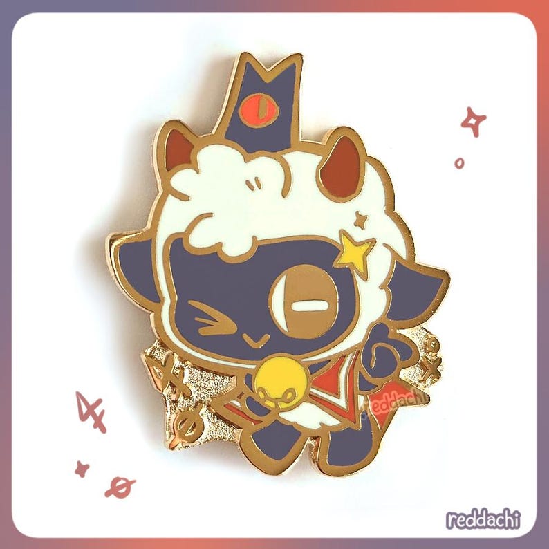May include: A gold-colored enamel pin featuring a cartoon lamb character with a crown, star, and red accents. The lamb has a dark blue face and white fur. The pin has the text "reddachi" on the bottom right.