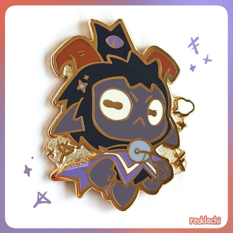 May include: A gold-colored enamel pin featuring a cartoon character with a dark blue face, purple accents, and a crown. The pin has a gold border and the text "reddachi" is visible.