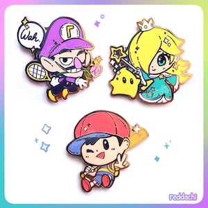 Puede incluir: Conjunto de tres pines de esmalte con personajes de dibujos animados. Un pin representa un personaje morado con una raqueta de tenis y la palabra "Wah". Otro muestra un personaje con una corona y una estrella. El tercer pin presenta un personaje con un bate de béisbol.