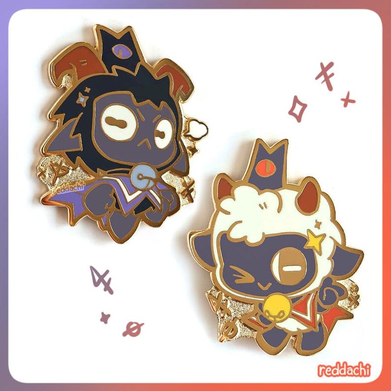 May include: Two enamel pins featuring cartoon lambs with gold accents. One lamb is dark with a crown, the other is white. Both have gold trim and are wearing capes. The pins have a cute, whimsical design.