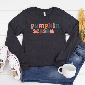 May include: A dark gray long-sleeved shirt with the text "Pumpkin season." in colorful retro lettering.