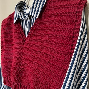 Op de afbeelding: Een bordeauxrode gebreide vest met een V-hals. De vest wordt gedragen over een gestreept shirt.