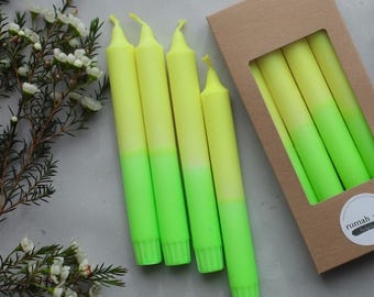 Könnte beinhalten: Neon-gelbe und grüne Ombre-Taperkerzen, einige außerhalb einer braunen Schachtel, andere darin. Die Kerzen liegen auf einer hellgrauen Oberfläche mit Grün. Auf der Schachtel steht 'rumah saya'.