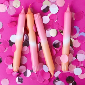 May include: Four ombre pink and orange candles on a pink background with pink, white, and gold confetti.