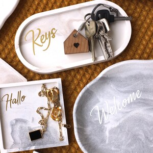 Könnte beinhalten: Fünf dekorative Tabletts mit marmorartigen Mustern. Die Tabletts sind mit den Worten "Keys", "Keys", "Hallo", "Welcome" und "Welcome" beschriftet.