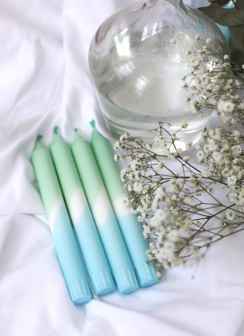 May include: Four ombre candles in shades of green, white, and blue. The candles are arranged in a row on a white surface.