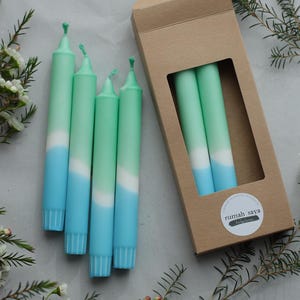 May include: Set of four ombre candles in shades of blue and green. The candles are packaged in a brown box with a white label that says "rumah saya".