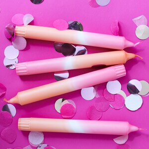 May include: Four ombre pink and orange birthday candles on a pink background with pink and silver confetti.