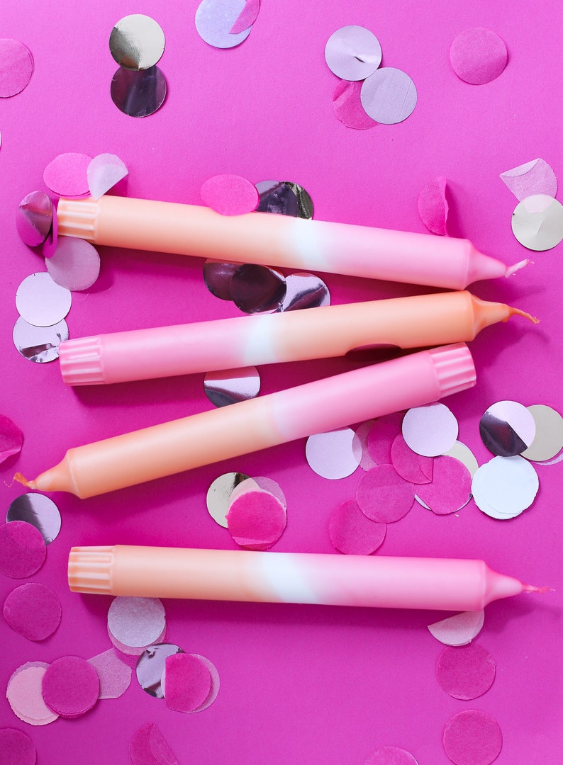 May include: Four ombre pink and orange birthday candles on a pink background with pink and silver confetti.