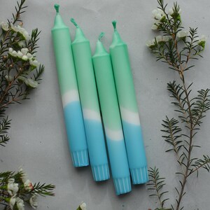 May include: Four ombre candles with a green to white to blue colour gradient. The candles are arranged in a row, with the green ends on the left and the blue ends on the right.