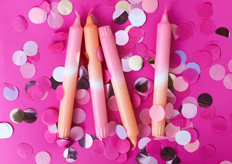 May include: Four ombre pink and orange candles on a pink background with pink, white, and gold confetti.