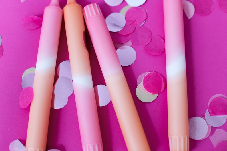 May include: Four ombre pink and orange candles on a pink background with pink and white confetti.
