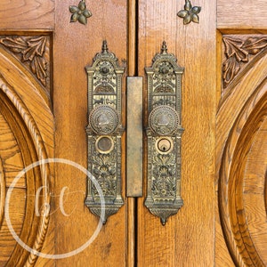 May include: Close-up of a pair of wooden doors with ornate brass hardware. The doors are a warm brown color with detailed carvings and decorative metal accents, including floral designs.