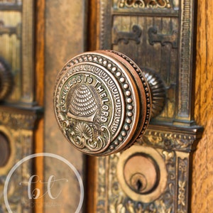 May include: A close-up of a vintage door knob with a brass finish. The knob features an ornate design with a beehive and the inscription "Holiness to the Lord".
