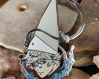 May include: A silver-colored enamel pin featuring a stylized anime-style character with light blue eyes, wearing a white hat and glasses. The pin has a light blue and black border with a D-shaped clasp.