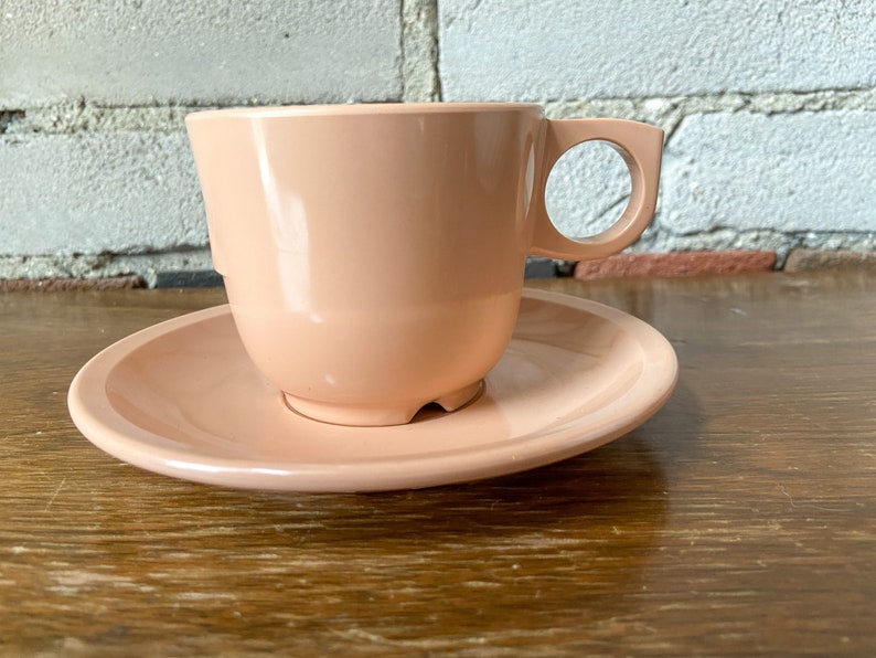 Puede incluir: Un juego de taza y platillo de color rosa p&aacute;lido. La taza tiene una forma redondeada y un asa. El platillo es de forma redonda y simple.