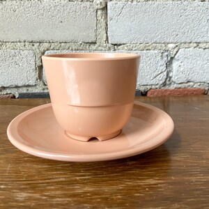 Puede incluir: Un juego de taza y platillo de cer&aacute;mica de color rosa p&aacute;lido. La taza tiene una forma redondeada y un acabado liso y brillante. El platillo es ligeramente m&aacute;s grande que la taza y tiene un dise&ntilde;o a juego.