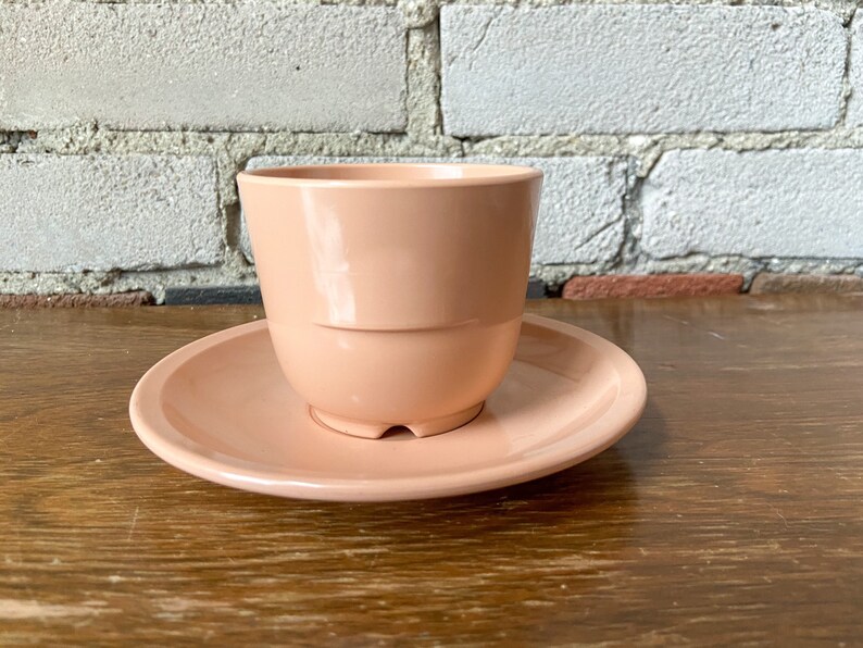 Puede incluir: Un juego de taza y platillo de cer&aacute;mica de color rosa p&aacute;lido. La taza tiene una forma redondeada y un acabado liso y brillante. El platillo es ligeramente m&aacute;s grande que la taza y tiene un dise&ntilde;o a juego.