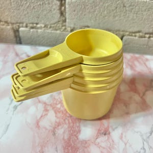 Può includere: Un set di misurini gialli, impilati. I misurini sono in plastica giallo chiaro e sono impilati. I manici sono angolati per una facile presa e misurazione. Sfondo: piano di lavoro in marmo.
