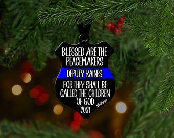 May include: Black and blue Christmas ornament with the text "Blessed are the peacemakers" and "Deputy Raines". The ornament also includes the text "For they shall be called the children of God" and "Matthew 5:9".