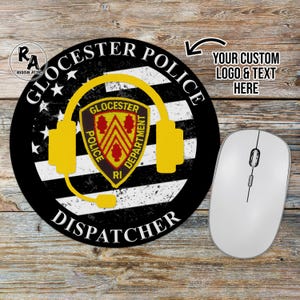 May include: Round black mousepad with a Gloucester Police Dispatcher design. The design includes a yellow headset, a shield with text, and the words "Gloucester Police Dispatcher". A white computer mouse is next to the mousepad.
