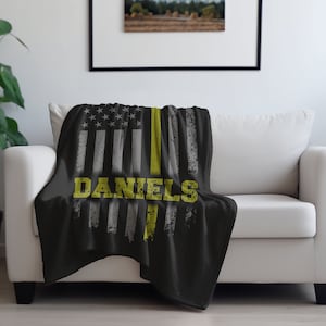 May include: Black and gray throw blanket with a thin yellow stripe down the center and a white and gray American flag design. The words "DANIELS" are printed in yellow on the blanket.