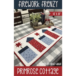 May include: A red, white, and blue quilted table runner featuring a design of four fireworks. The table runner is 18 inches by 39 inches and is titled "Firework Frenzy" with the designer's name, "Primrose Cottage", below.