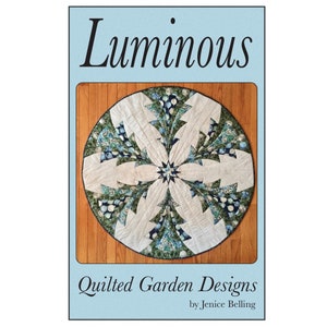 May include: A circular quilt with a floral pattern, using white, blue, and green fabrics. The quilt has a central star design and a border. The image displays the text "Luminous" and "Quilted Garden Designs".