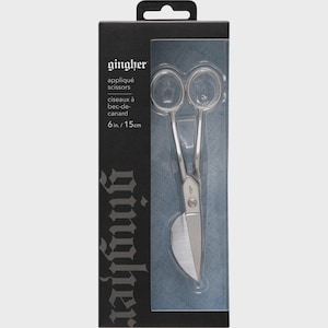 May include: Gingher appliqué scissors in a black retail box. The silver-colored metal scissors feature a duckbill blade design and two finger loops. The packaging displays the text Gingher, appliqué scissors, and 6 in. in white lettering.