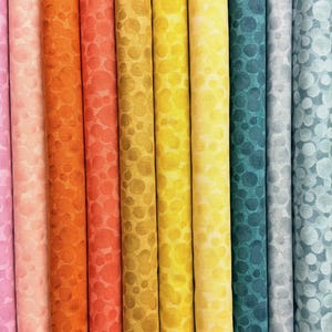 May include: A selection of fabric rolls in a variety of colours, each with a pattern of overlapping circles. The colours include reds, pinks, oranges, yellows, blues, and greens. The fabric appears to be cotton or a similar material.
