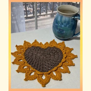 May include: Crochet pattern for a heart-shaped sunflower coaster. The coaster is made with brown and yellow yarn and has a heart-shaped center. PDF Instant Download.