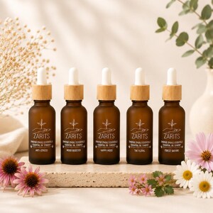 May include: Five amber glass dropper bottles with bamboo collars and white droppers, each labelled ZARITS with a hand and sprout icon. The labels read Anti-Stress, Mood Booster, Happy Mood, The Floral, and Forest Bathing in white text.
