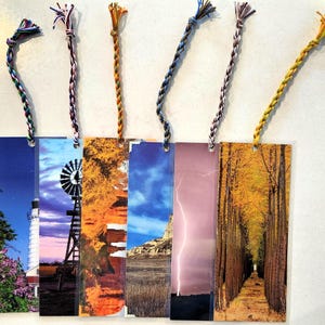 May include: Set of six colorful bookmarks with different images. The images include a lighthouse, a windmill, a canyon, a stormy sky, a row of trees, and a field of trees.