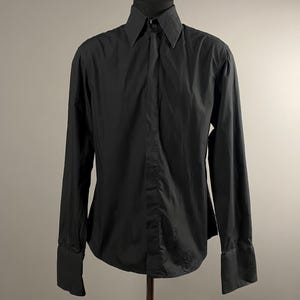 May include: A black long-sleeved button-up shirt with a pointed collar and a single button cuff.