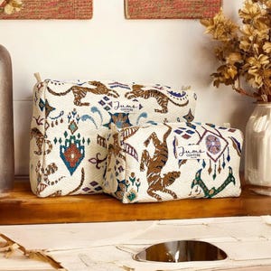 Peut inclure: Trois trousses de toilette en tissu blanc avec un motif géométrique coloré et un imprimé de tigre brun. Les trousses portent l'inscription "Jumo Couture".