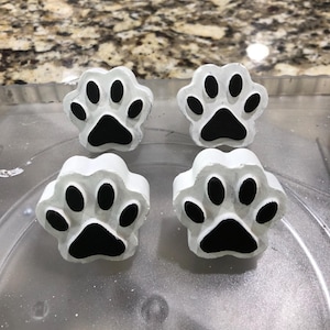 May include: Four white paw print-shaped decorative items with black paw pads. The items are arranged in a square formation, showcasing a pet-themed design. The paw prints are likely used as decorative knobs or drawer pulls.
