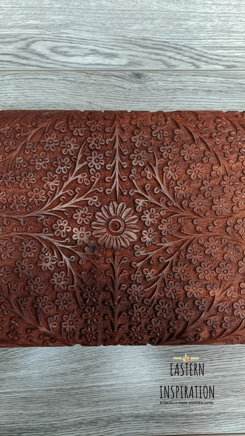 Puede incluir: Una caja de madera con intrincados tallados florales. La caja est&aacute; hecha de madera marr&oacute;n oscura y tiene un dise&ntilde;o rico y detallado. Los tallados son de estilo tradicional y presentan una variedad de flores y hojas.