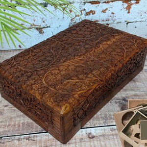 Puede incluir: Una caja de madera con intrincados tallados florales. La caja est&aacute; hecha de madera marr&oacute;n oscura y tiene una forma rectangular. Los tallados son detallados y cubren toda la superficie de la caja.