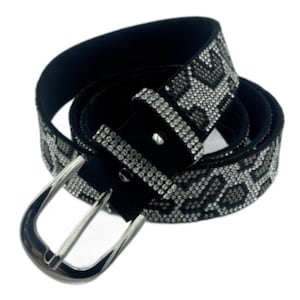 May include: Black belt with a silver buckle and a pattern of silver rhinestones. The belt is made of black suede material and has a classic design. The rhinestones are arranged in a geometric pattern.