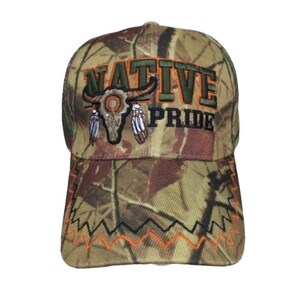 Puede incluir: Gorra de béisbol de camuflaje con las palabras "NATIVE PRIDE" bordadas en naranja y negro. La gorra presenta un diseño de calavera de toro y plumas. El borde tiene un patrón en zigzag en negro y naranja.