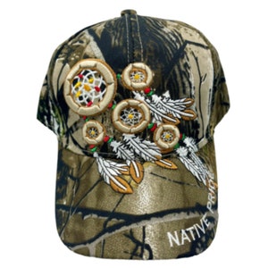 May include: A camouflage baseball cap with an embroidered design of dreamcatchers and feathers. The cap has the text "NATIVE PRIDE" on the side.